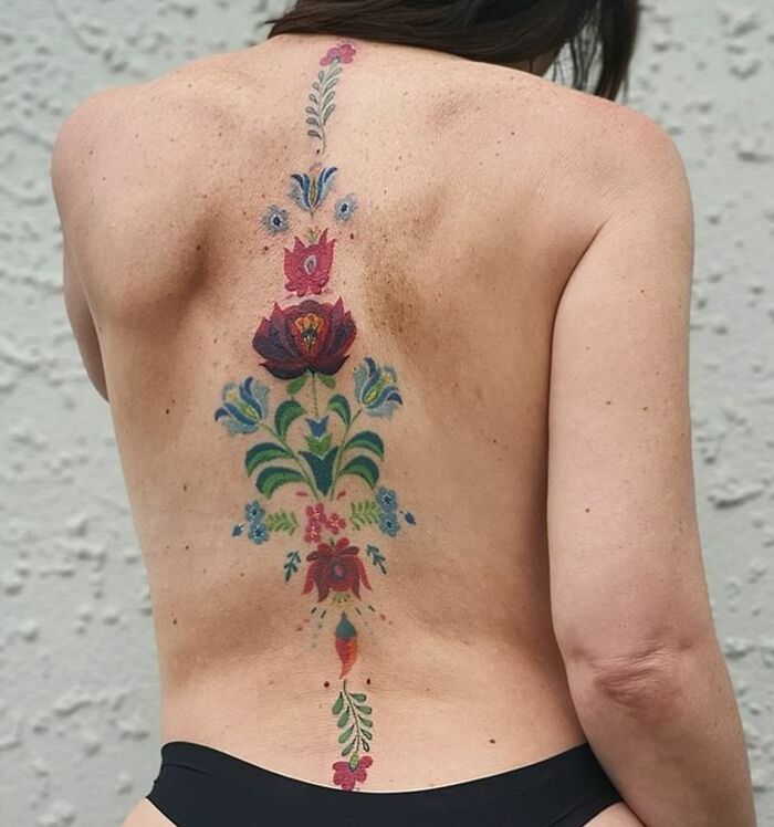 Colorful floral spine tattoo design on woman's back, showcasing elegant tattoo ideas.
