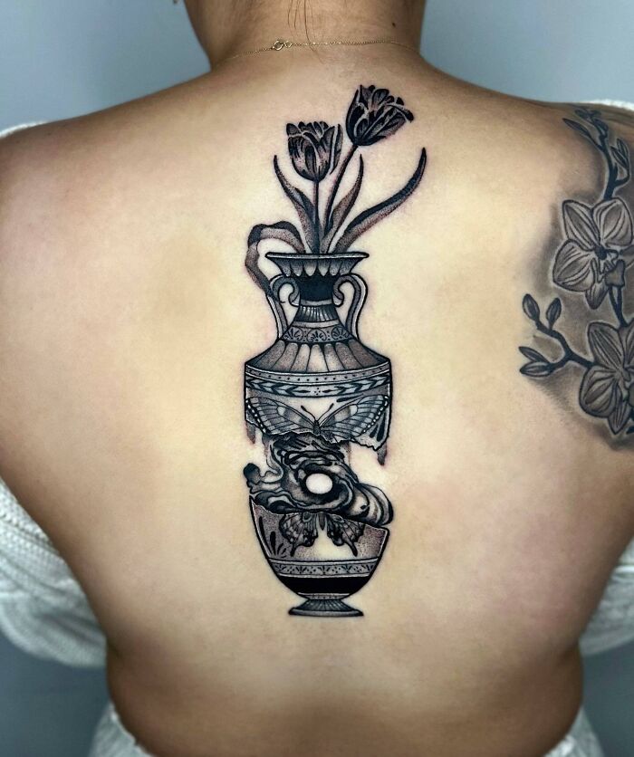 Elegant spine tattoo featuring a detailed vase with flowers and ornate designs.