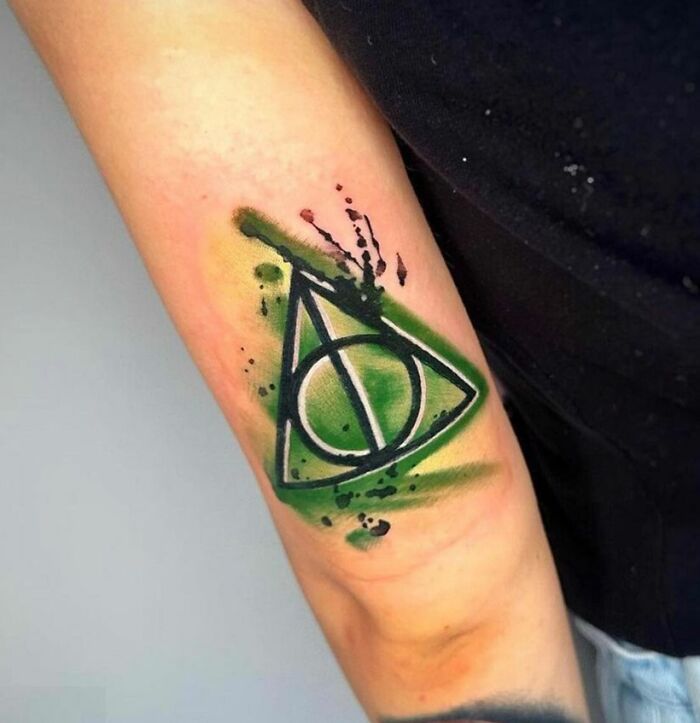 Harry Potter tattoo of the Deathly Hallows symbol with green watercolor effect on forearm.