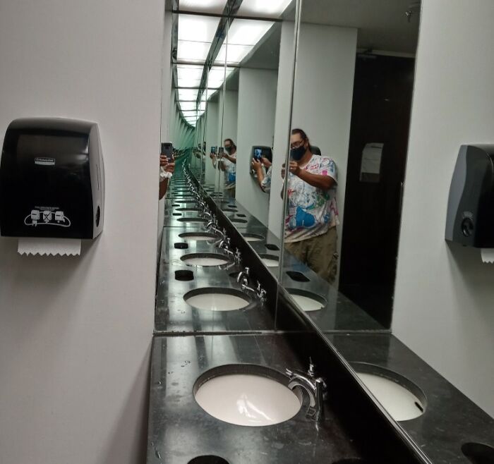 Multiple mirror reflections of a man taking a picture in a bathroom 