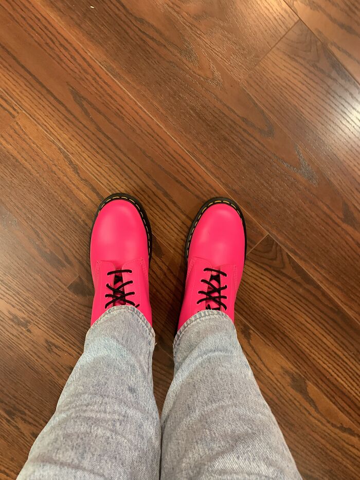 Bright pink boots with black laces on a wooden floor, showcasing a unique shoe style.