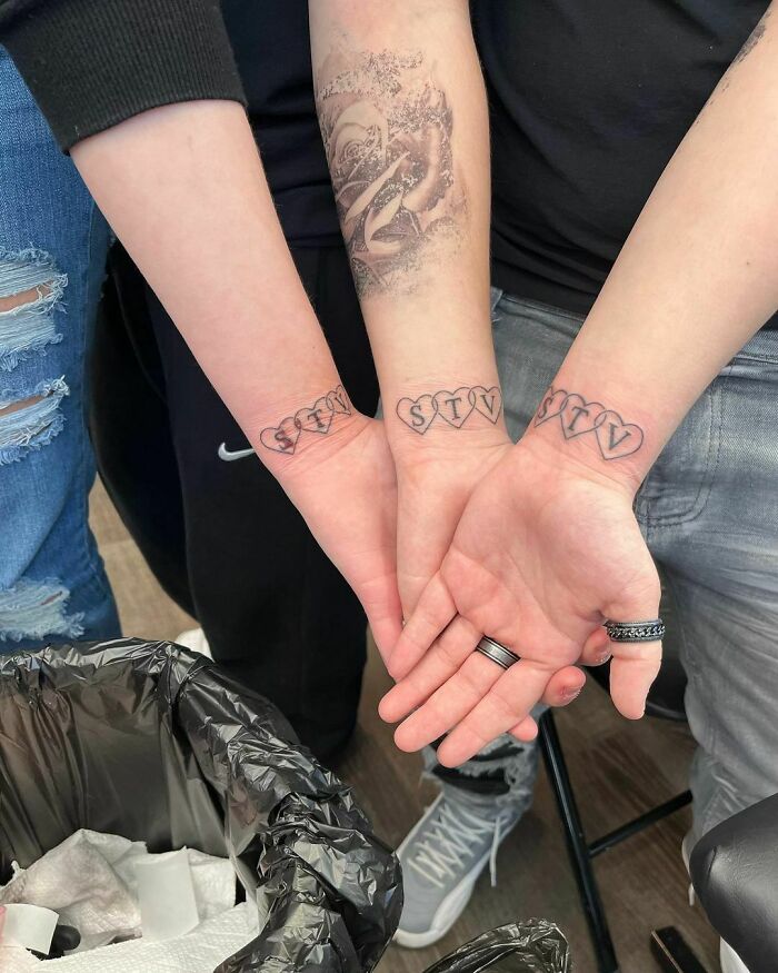Matching wrist tattoos in the shape of tree hearts with letters in them
