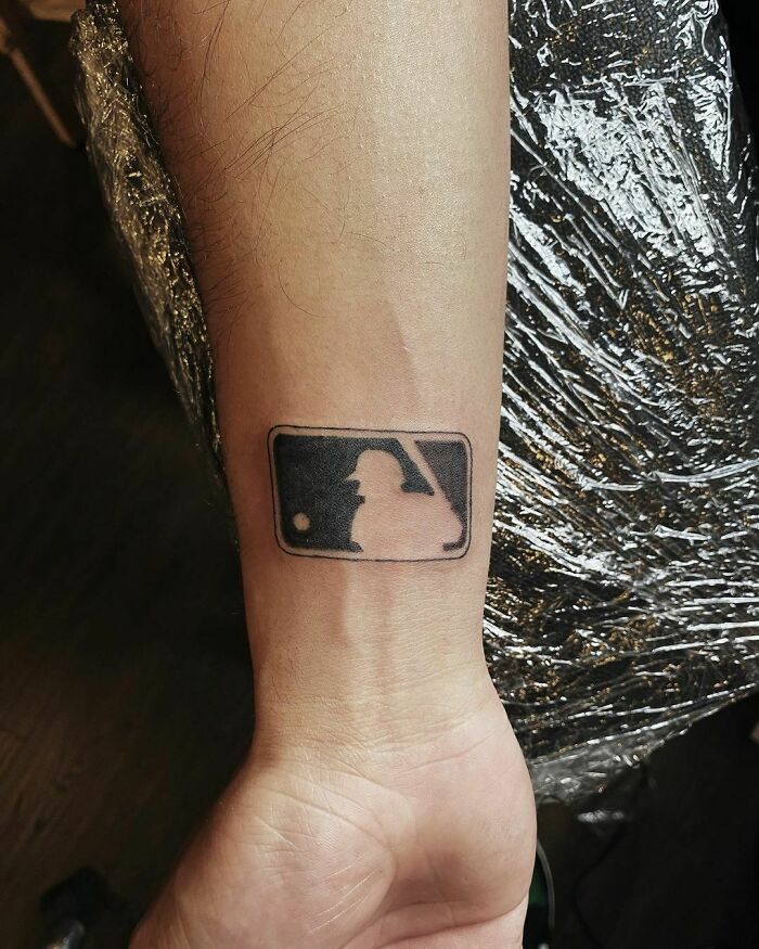 Wrist tattoo depicting a silhouetted baseball player in black ink on a person's arm.