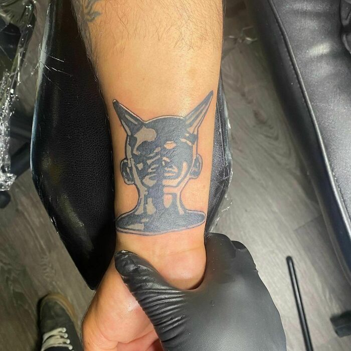 Black ink wrist tattoo featuring a horned, abstract figure design.
