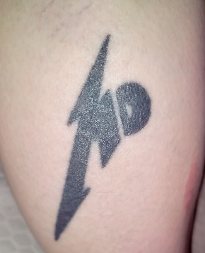 Tattoo featuring a bold, stylized lightning bolt and circle design on skin.