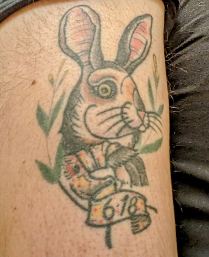 Tattoo of a colorful cartoon rabbit with big ears and a scroll featuring numbers, surrounded by green accents.