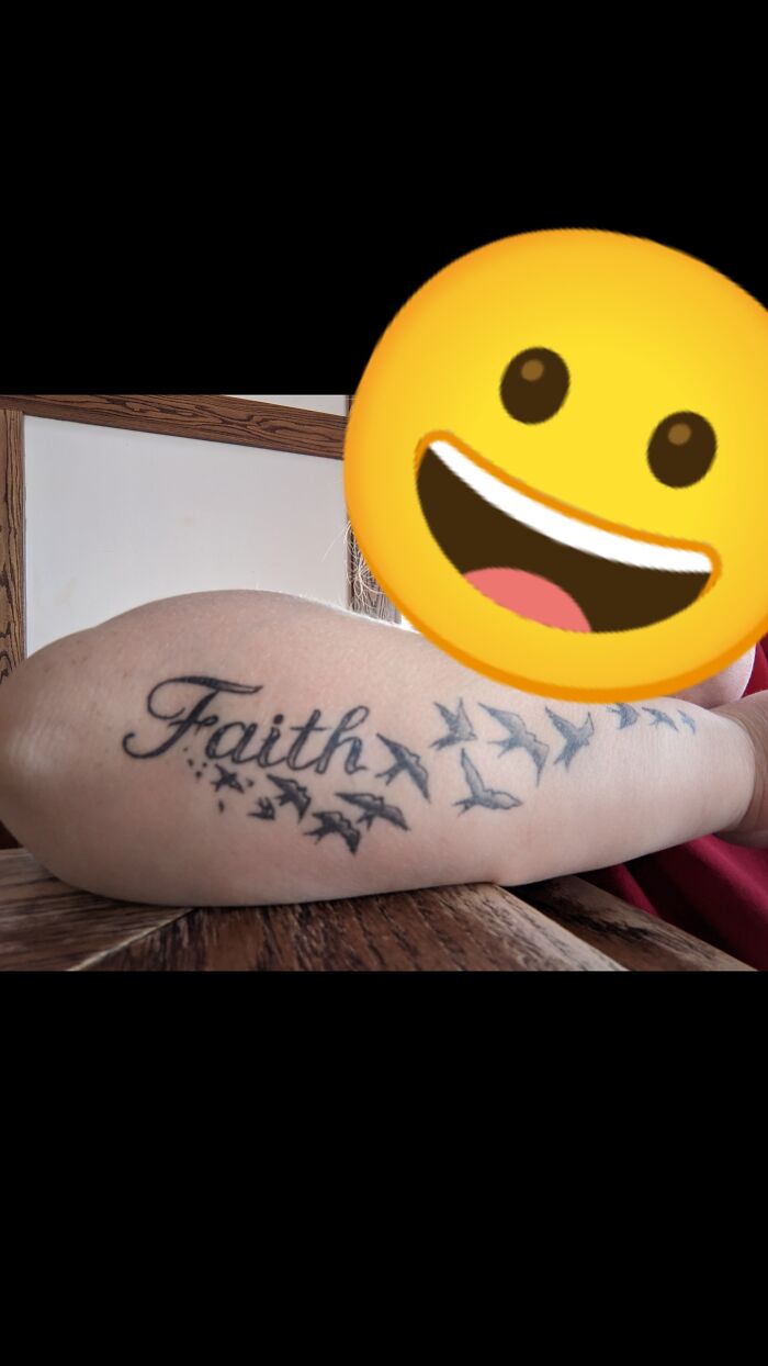 Arm tattoo of the word "Faith" with flying birds design on a wooden table background.