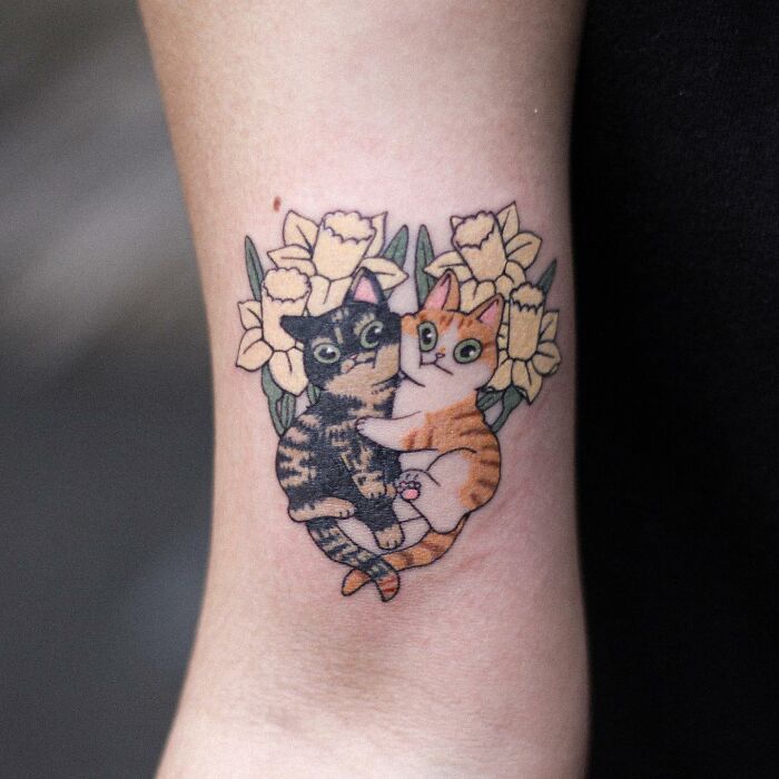 Adorable animal-themed tattoo of two cats surrounded by yellow flowers.