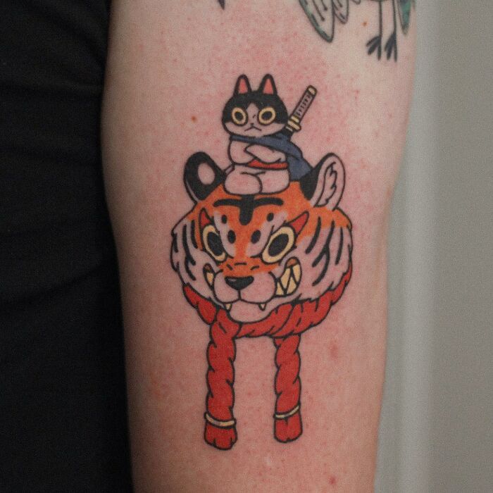 Tattoo of a cute animal-themed design featuring a cat with a sword riding on an illustrated tiger.