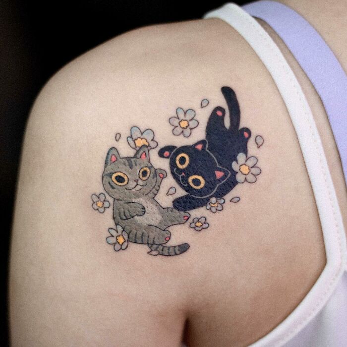 Animal-themed tattoo of playful cats surrounded by flowers on a person's shoulder.