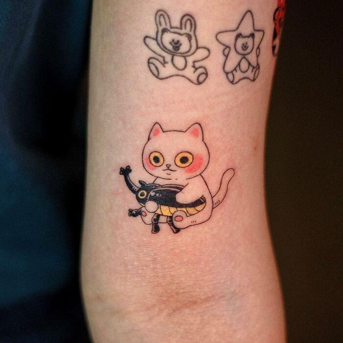 Adorable animal-themed tattoo of a cat holding a small doll on forearm.