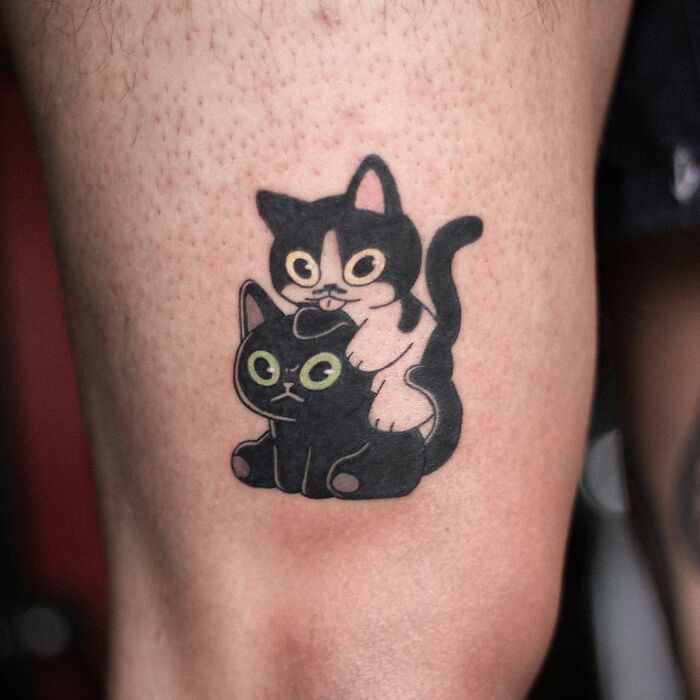 Adorable animal-themed tattoo of two cute cartoon cats on a person's leg.