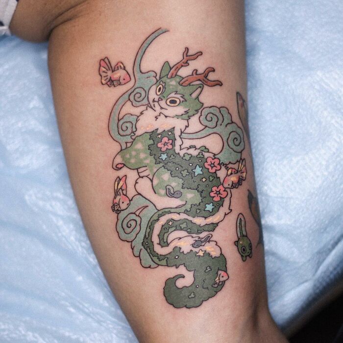 Adorable animal-themed tattoo of a dragon-like creature with whimsical details and vibrant colors on a person's arm.