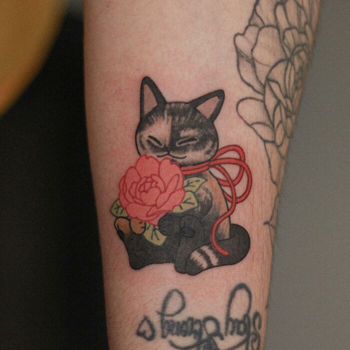 Adorable animal-themed tattoo of a cat holding a pink flower, designed by a tattoo artist.