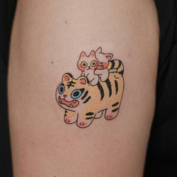 Cute animal-themed tattoo featuring a cartoon-style tiger with a cat on its back.