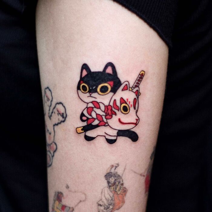 Adorable animal-themed tattoo of a cartoon cat with a mask, showcasing colorful and playful design on an arm.