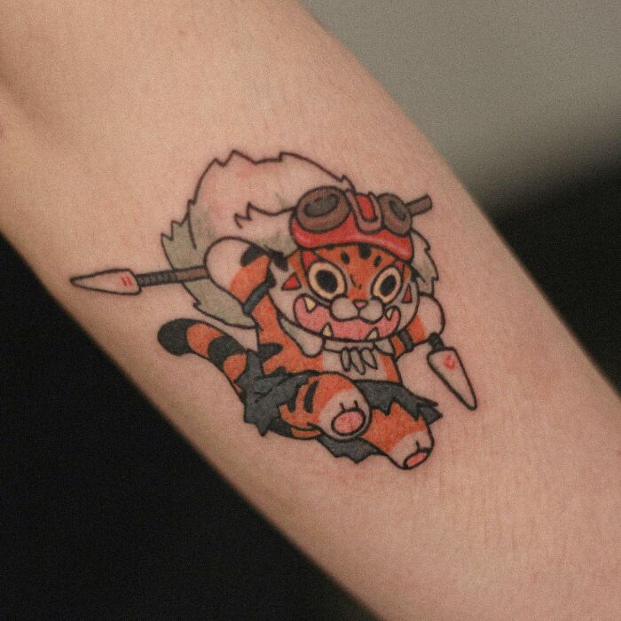 Adorable animal-themed tattoo of a cartoon tiger with goggles on an arm.