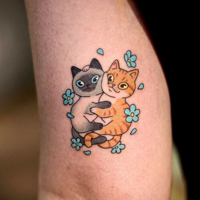 Adorable animal-themed tattoo of two hugging cats with blue flowers.