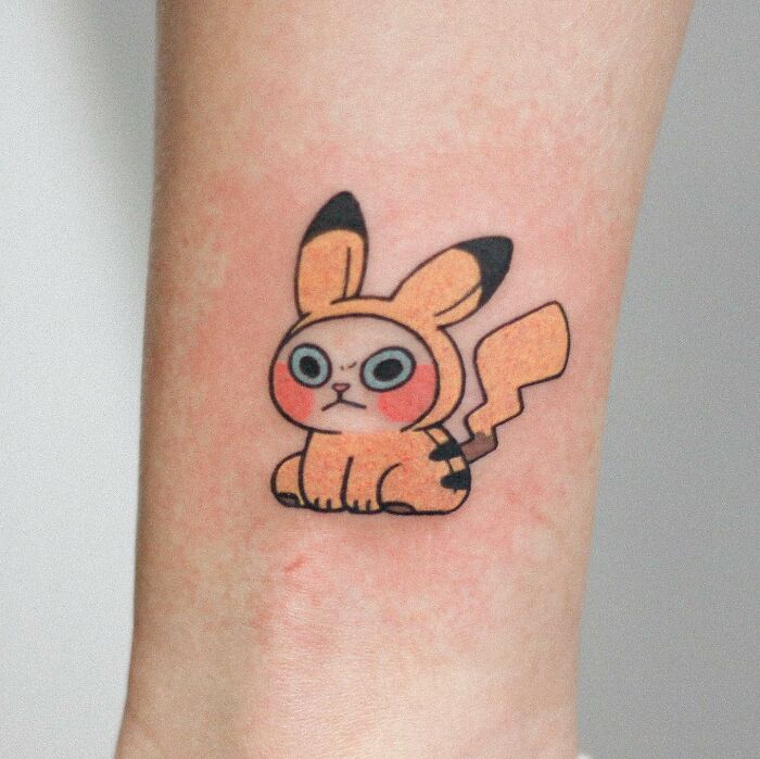 Adorable animal-themed tattoo of a cute creature with large eyes and a lightning-shaped tail on skin.