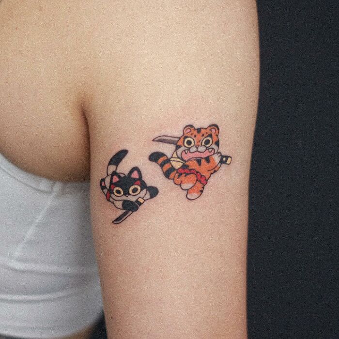 Adorable animal-themed tattoo featuring a playful cat and tiger on a person's arm.