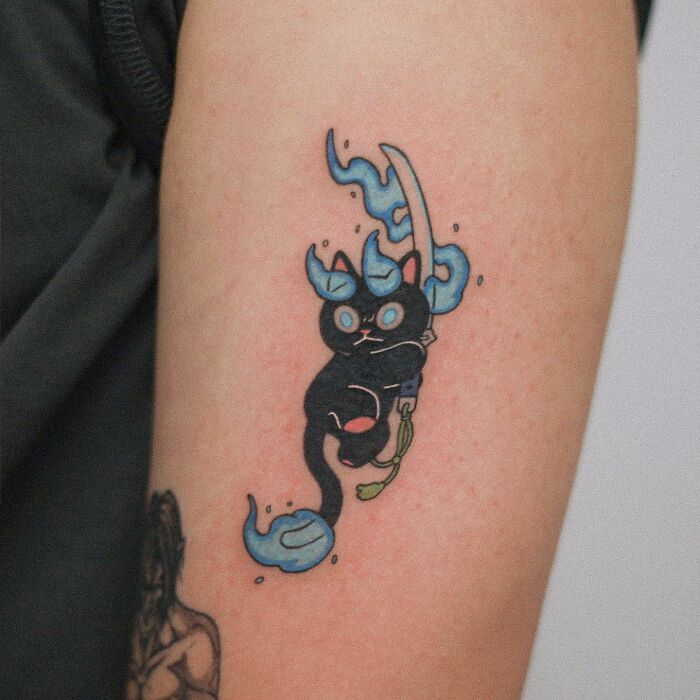 Adorable animal-themed tattoo of a cartoon black cat with blue flames on an arm.