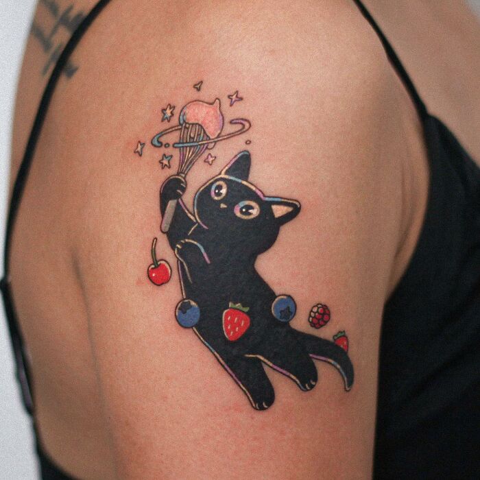 Tattoo of a cute black cat with fruit-themed designs on an arm, showcasing animal-themed tattoo artistry.