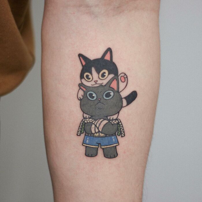 Adorable animal-themed tattoo of two cute cartoon cats on a person's forearm.