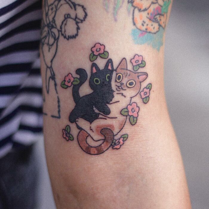 Tattoo of two cats surrounded by flowers, showcasing adorable animal-themed design on a person's arm.