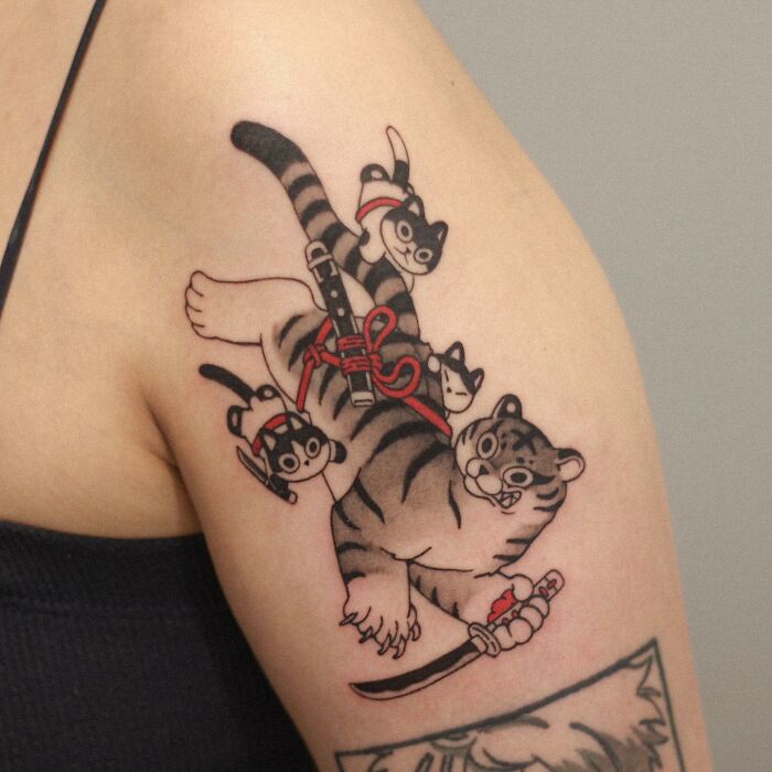 Tattoo of a cartoon tiger with kittens on top on a person's arm, showcasing adorable animal-themed design.