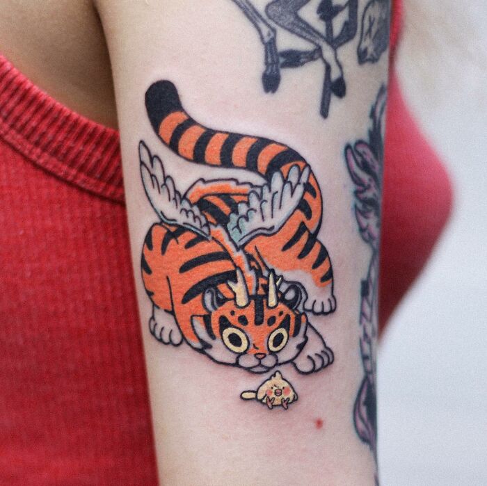 Animal-themed tattoo of a mythical tiger with wings and playful expression on a person's arm.
