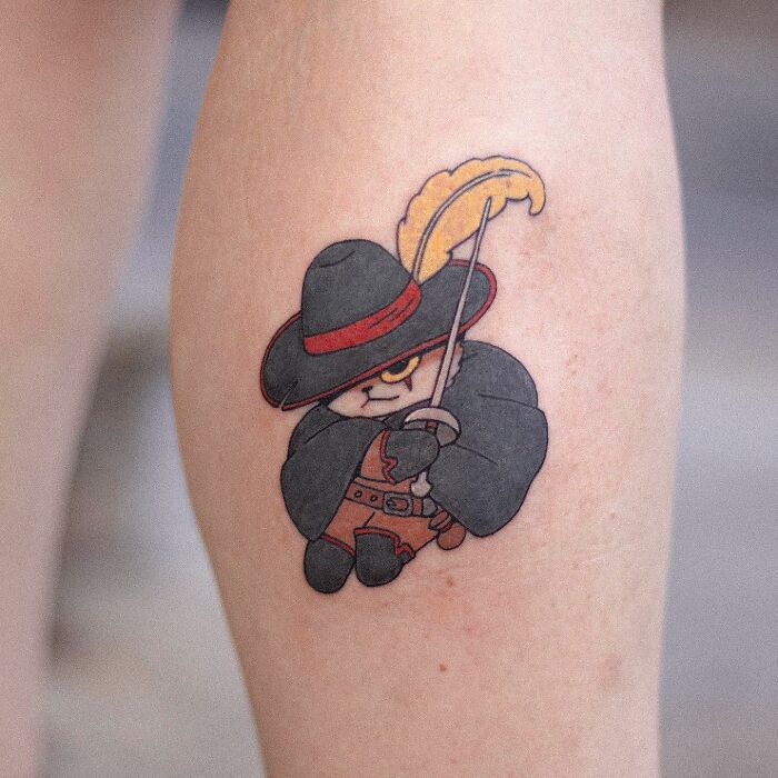 Adorable animal-themed tattoo of a cute character in a cloak and hat on a person's leg.