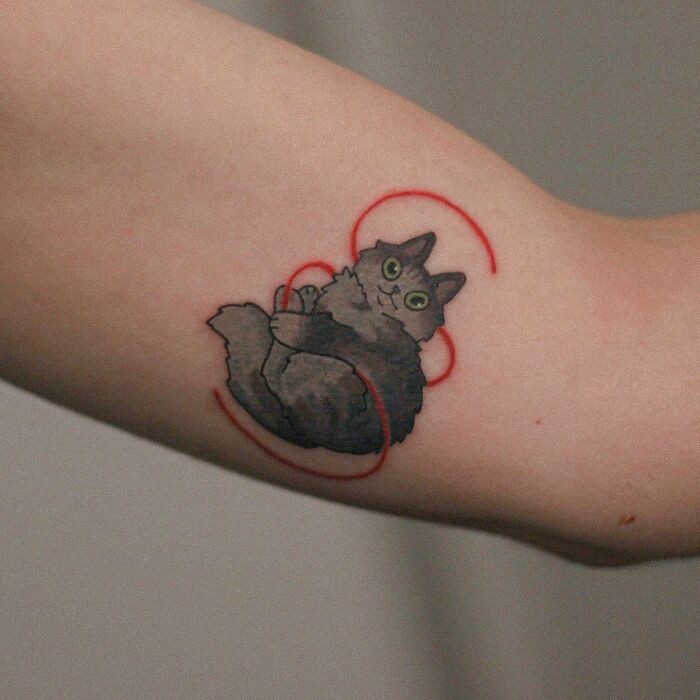 Adorable animal-themed tattoo of a playful cat with a red yarn on an arm.