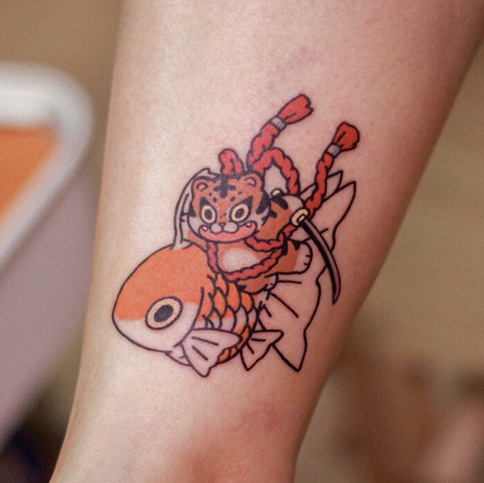 Adorable animal-themed tattoo of a playful tiger on a fish, designed by a creative tattoo artist.