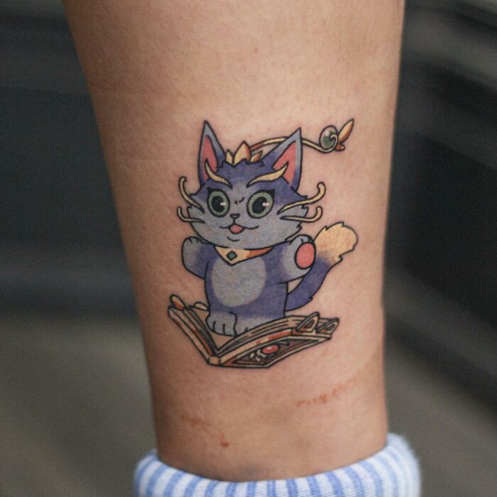 Adorable animal-themed tattoo of a colorful cartoon cat on a person's arm.