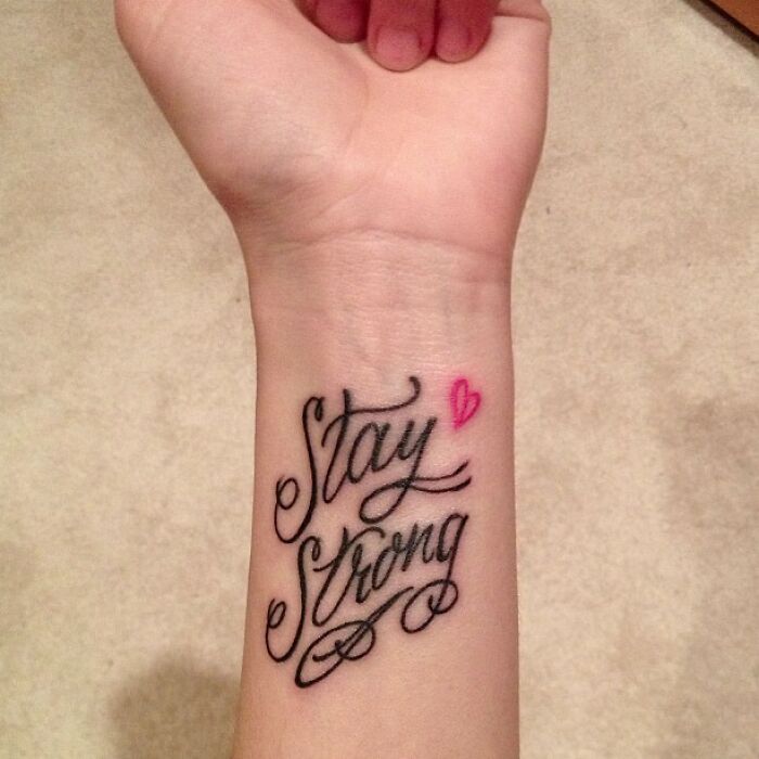 Phrase and pink heart tattoo on wrist