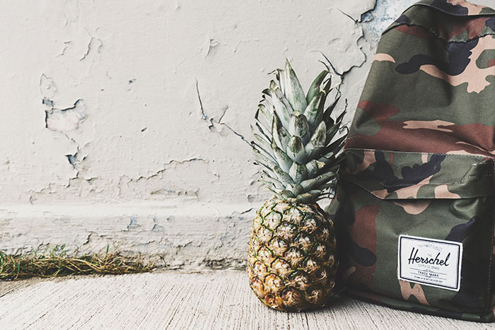 Pineapple Fruit Beside Black, Brown, and Beige Herchel Camouflage Backpack