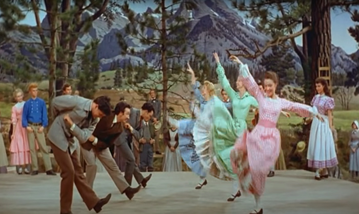 Three women and three man are dancing and many people in their background