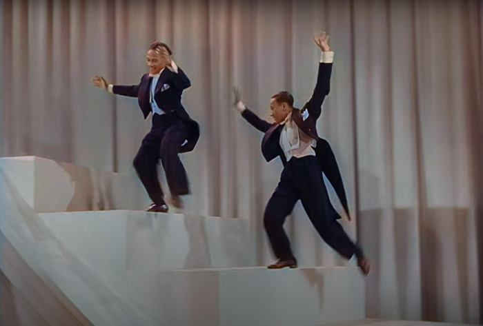 Nicholas Brothers in a classy outfit dancing on the big white stairs and the light curtains in the background
