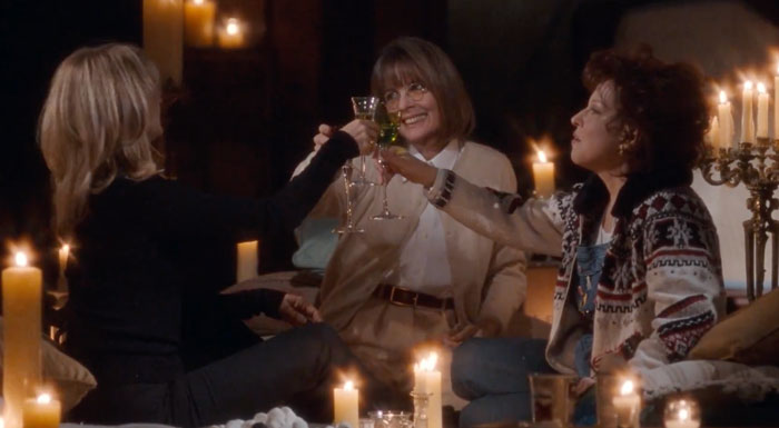 Three women celebrating friendship, toasting with wine glasses in a cozy candle-lit setting.