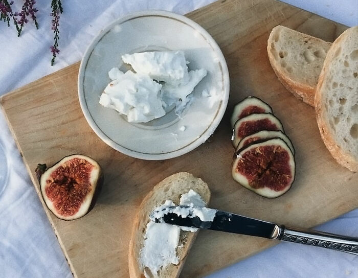 cheese on the plate near the piece of white bread with knife and figs