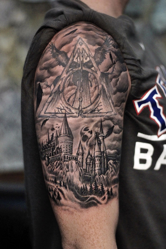 Harry Potter tattoo featuring Hogwarts and the Deathly Hallows on someone's upper arm.
