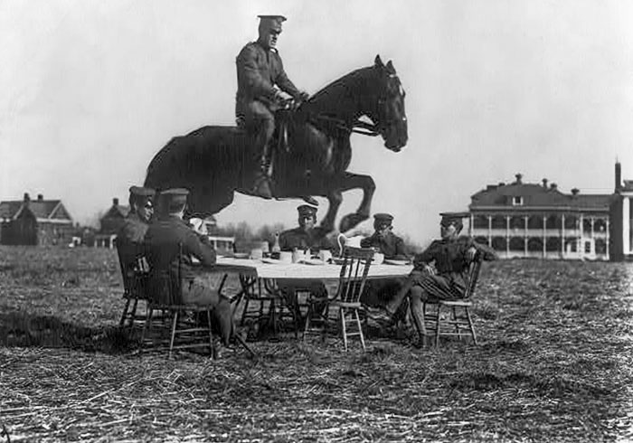 U.S. Army Men Seated Around The Table, While One On Horseback Jumping Over It