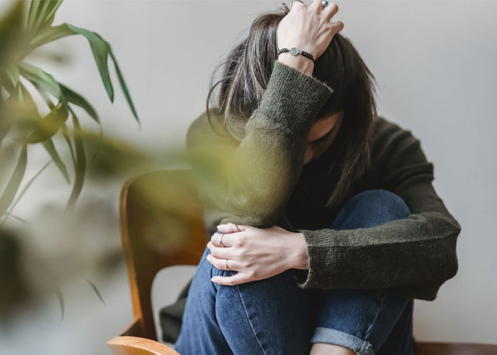 Stressed woman sitting, hand on head, contemplating issues surrounding MIL's desire for grandkid's footprint tattoo. Stressed woman sitting, hand on head, contemplating issues surrounding MIL's desire for grandkid's footprint tattoo.