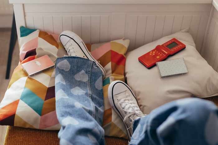 Person lying in the bed and wearing blue jeans with white shoes