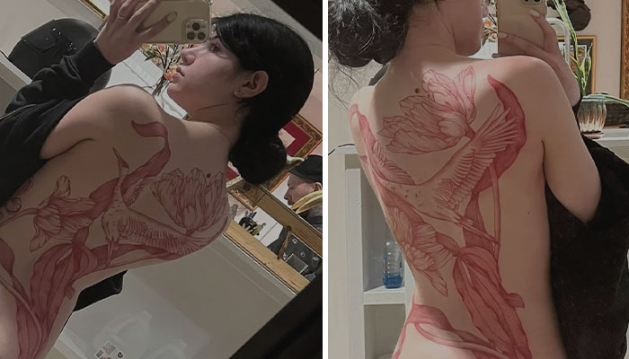 A person showing an intricate floral red ink tattoo on their back in a mirror reflection.