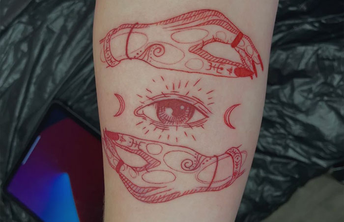 Red ink tattoo featuring an artistic design of an eye with intricate details on skin.
