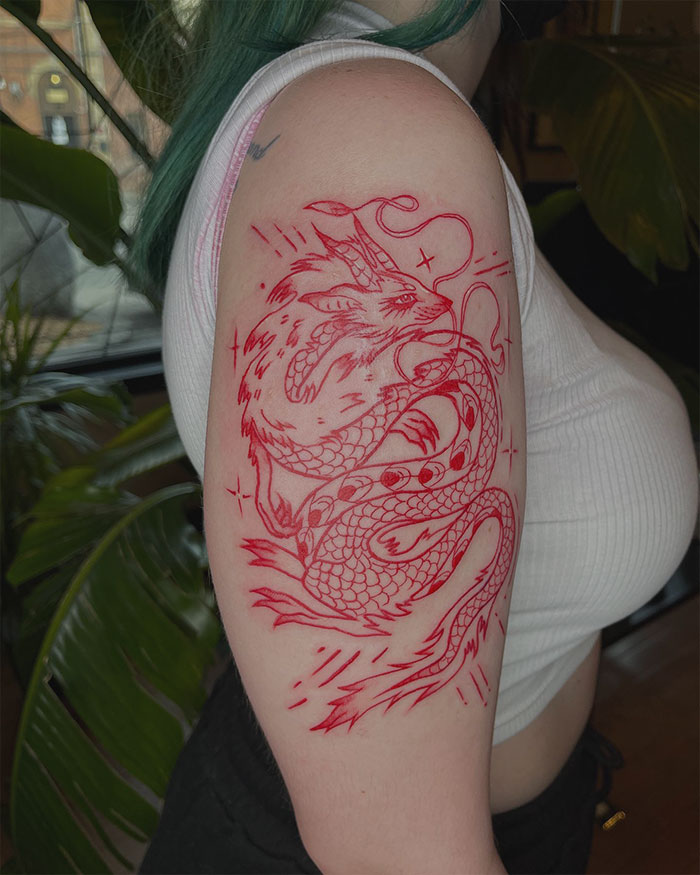 Red ink tattoo of a detailed dragon design on an arm, showcasing intricate line work.