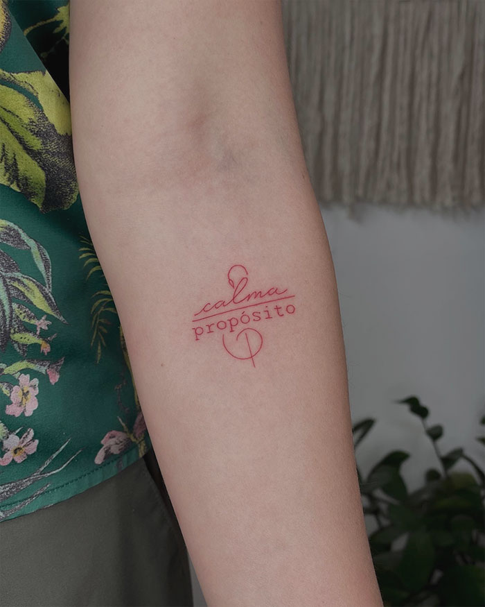 Arm with red ink tattoo showing text "calma propósito" on a floral background.