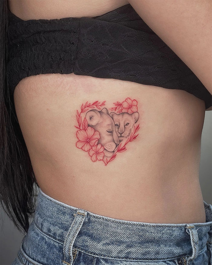 Red ink tattoo of two lions surrounded by flowers on side torso.