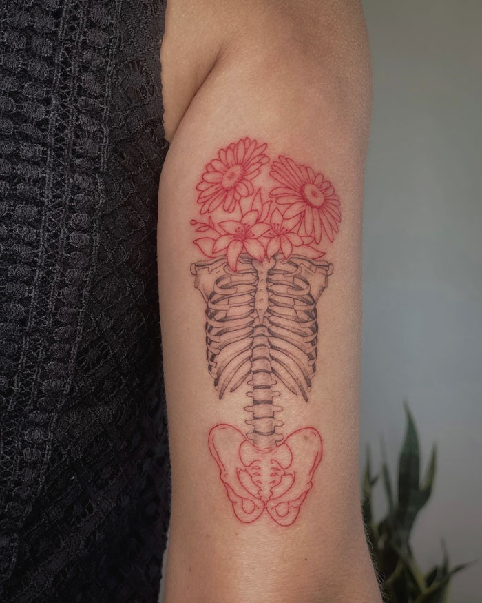 Red ink tattoo of an artistic ribcage with flowers on arm, showcasing a unique design in intricate detail.
